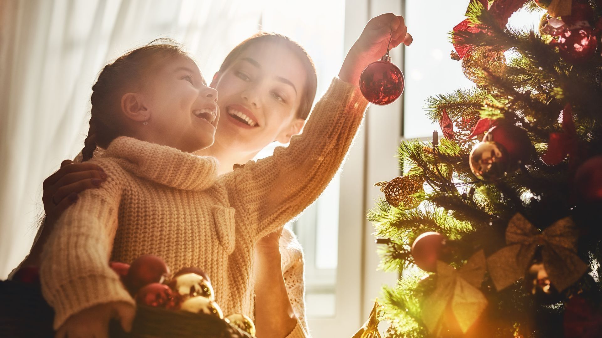mother helping her daughter hang chritmas tree ornaments