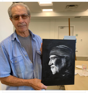 A man in a blue shirt is holding a painting of a man with a beard
