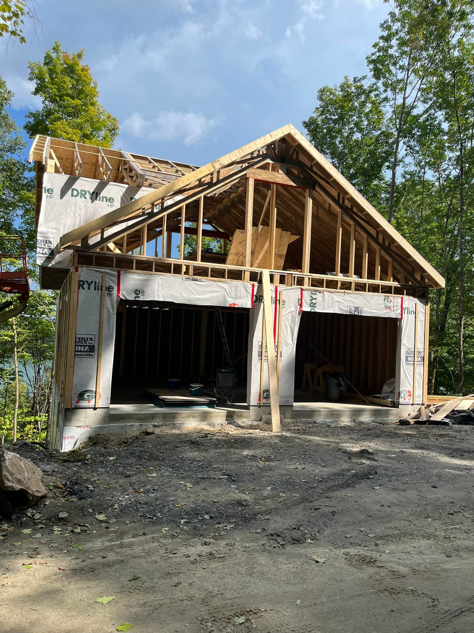 Garage en construction à l'extérieur, avec deux travées, une structure en bois et un toit partiellement construit.