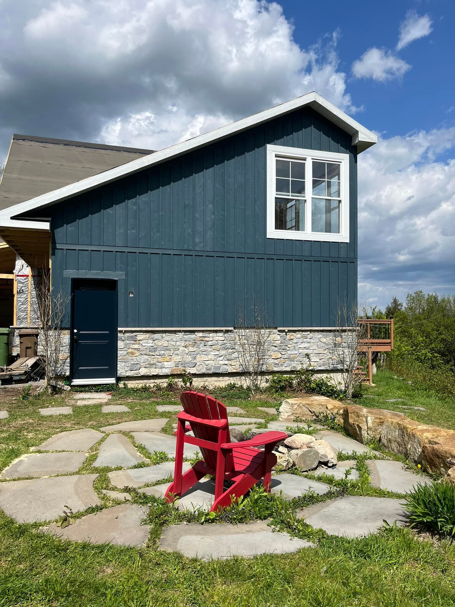 Chaise Adirondack rouge sur une terrasse en pierre devant un bâtiment aux murs bleus et aux fenêtres à encadrement blanc.