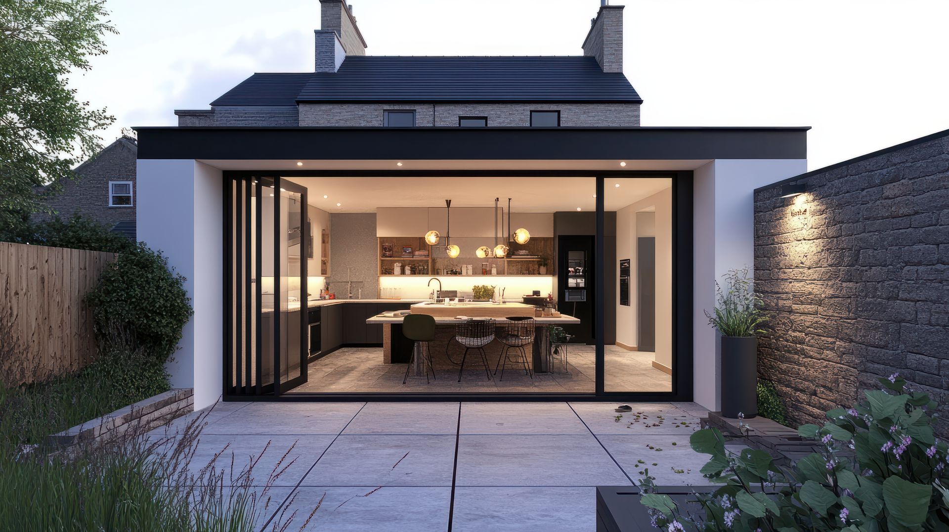 Extension de cuisine moderne avec portes vitrées pliantes, terrasse en pierre et éclairage extérieur.