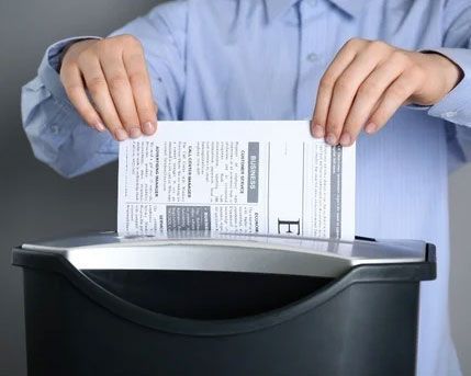 Hands placing a document into a black shredder bin