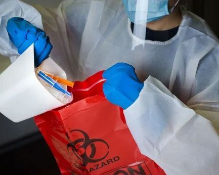Person in blue gloves placing a medicine box into a red biohazard bag at a healthcare site