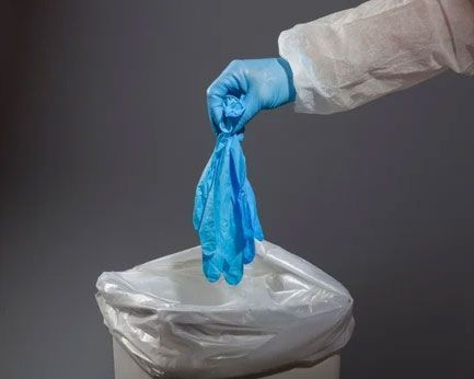 Gloved hand dropping a blue disposable glove into a trash bin