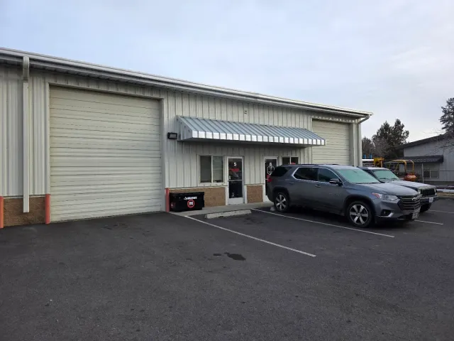 A single-story commercial metal building with two garage doors and a central entrance, with two SUVs parked in front | SP Auto and Transmission World