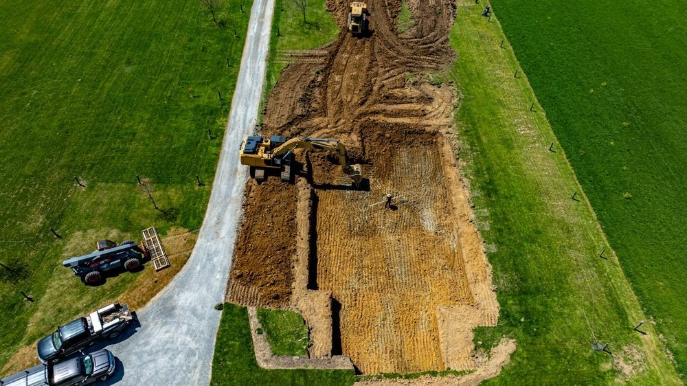 Construction excavators digging a long trench beside a paved road through green fields