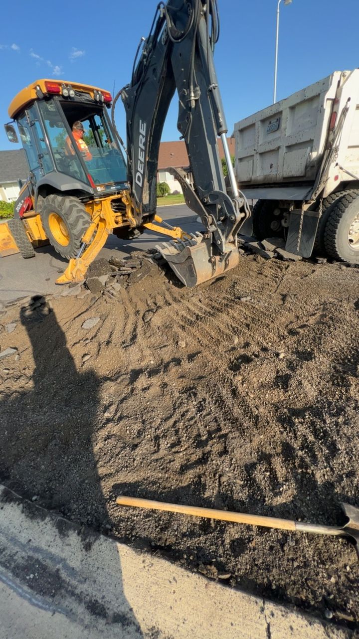 Excavator and dump truck loading dirt at a roadside construction site