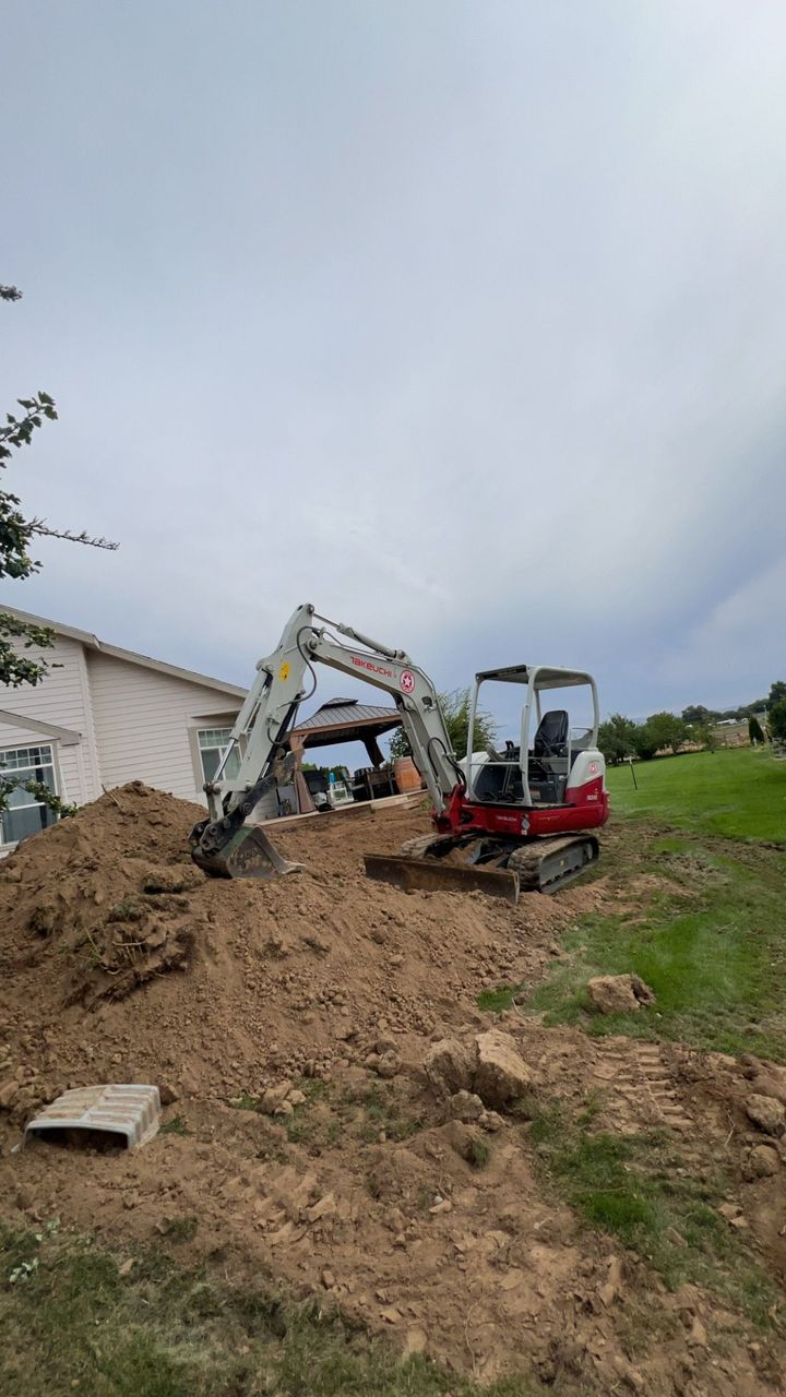 Excavator clearing dirt on a sloped grassy construction site under a cloudy sky