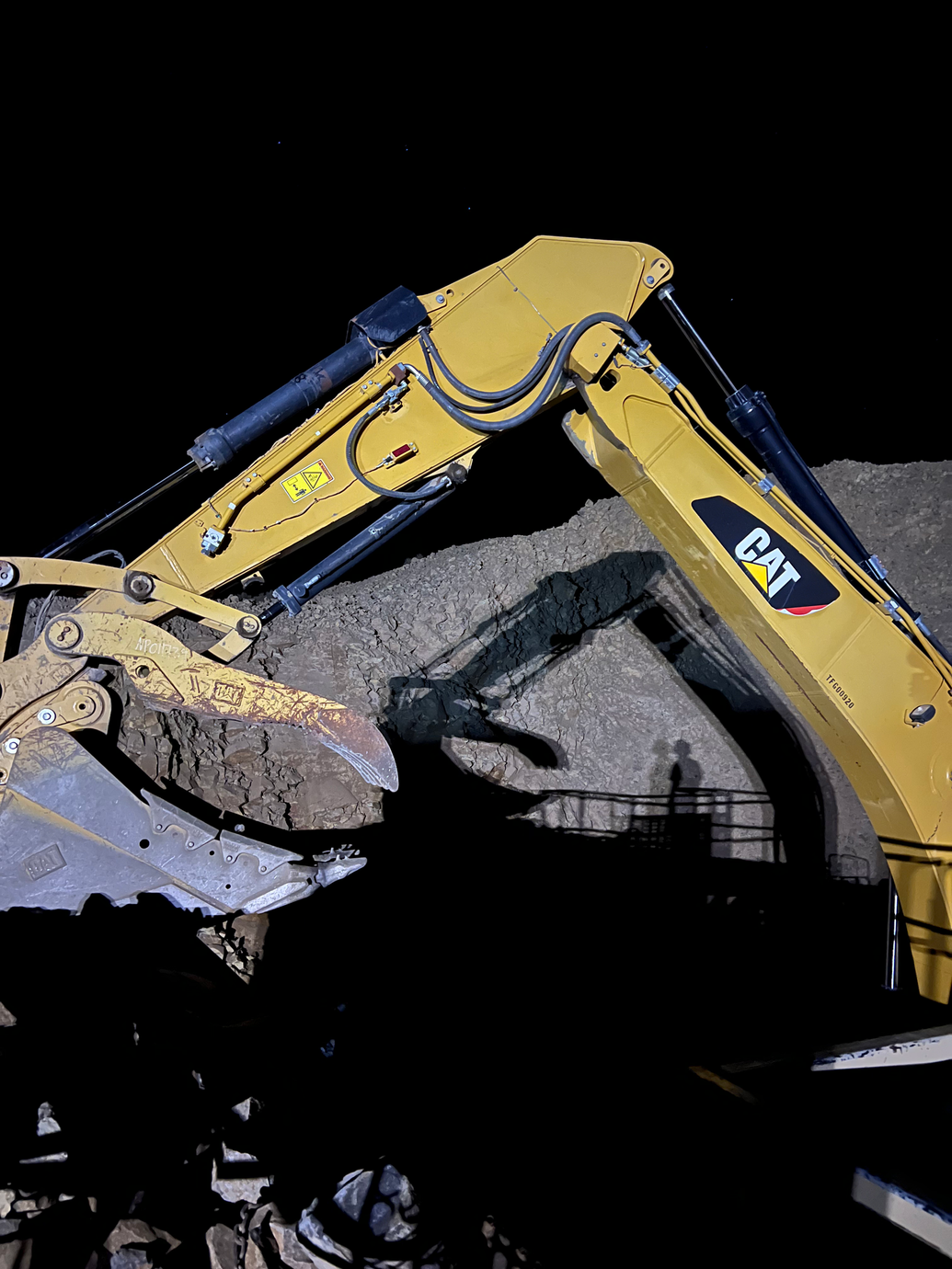 Yellow excavator arm digging rubble at night against a dark background
