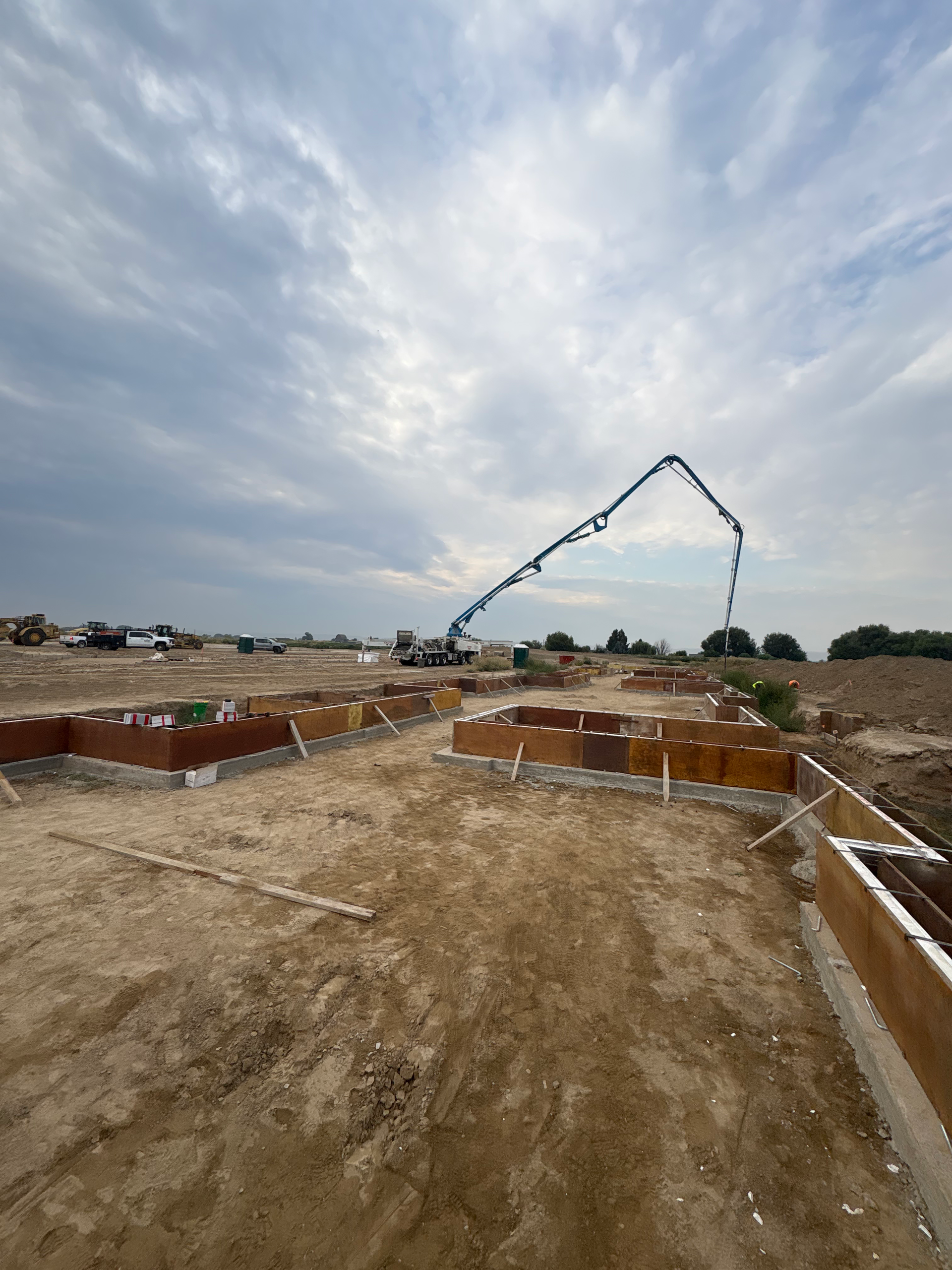 Construction site with concrete foundation walls and a pump truck pouring concrete under a cloudy sky