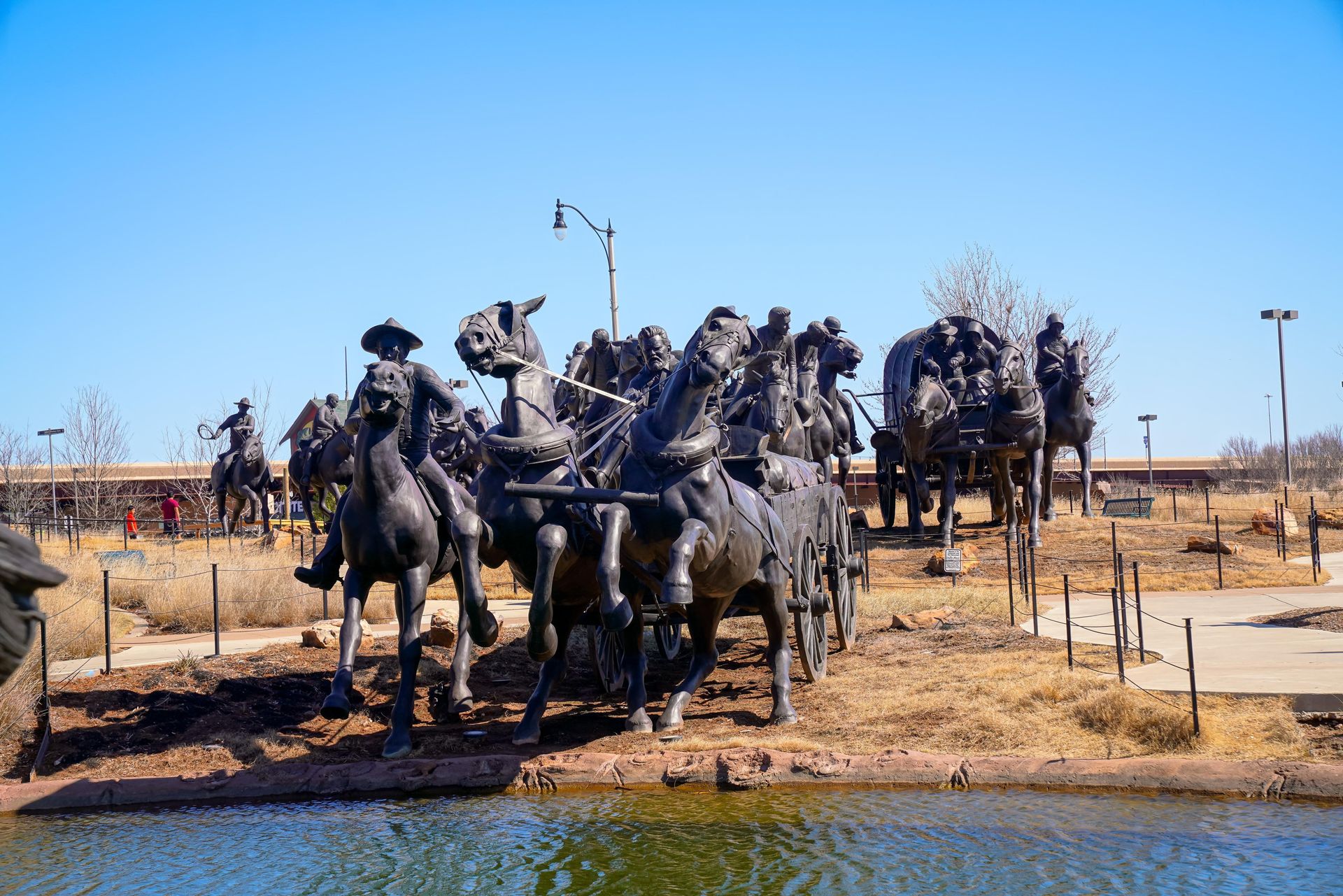 Bronze cowboy statue group on horses beside a pond under a clear blue sky