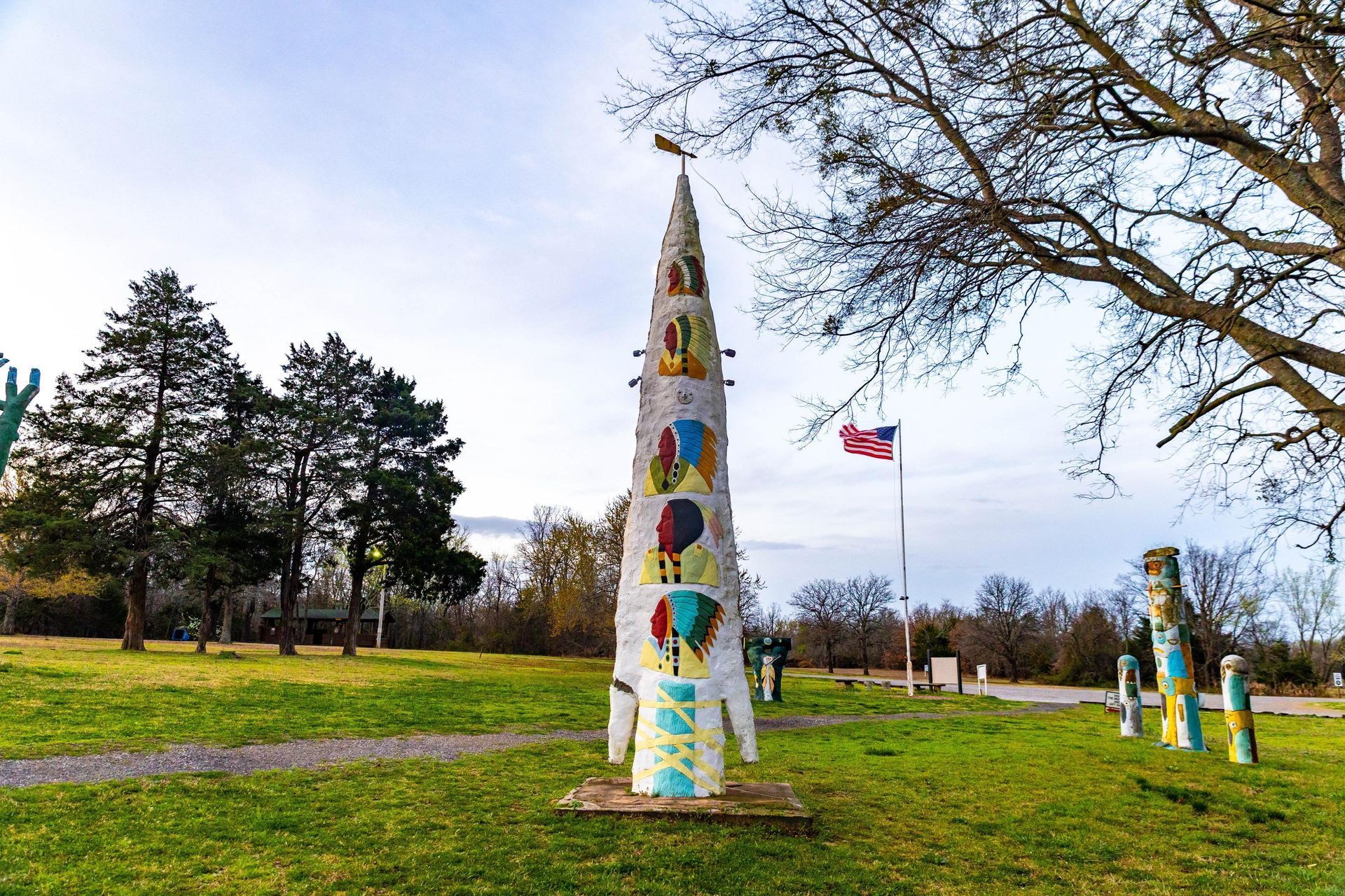 Colorful painted sculptures in a grassy park with trees and a flag under a cloudy sky