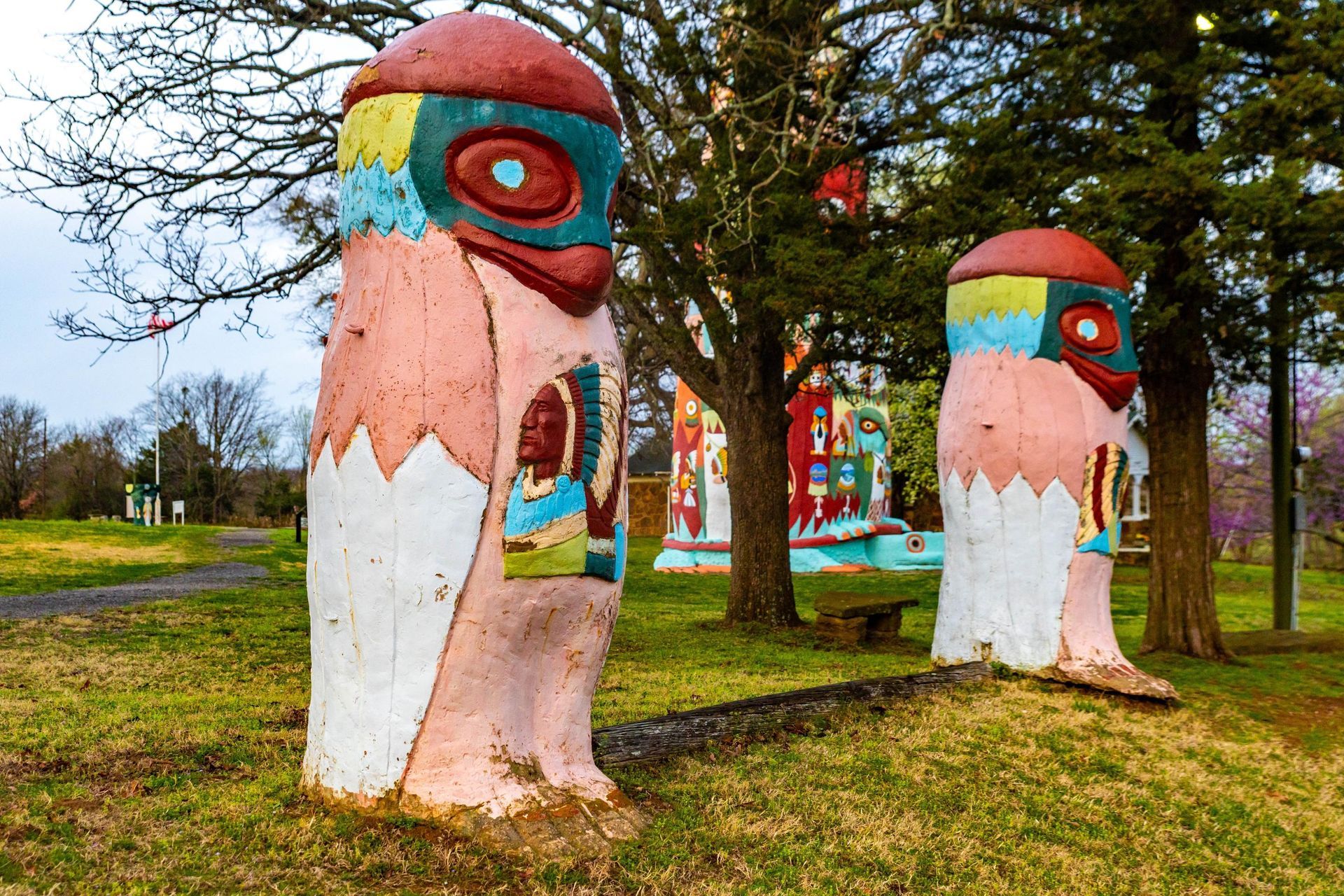 Colorful carved wooden totem poles in a grassy park with trees and a path in the background