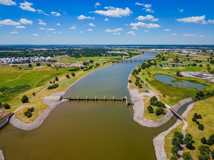Aerial view of a river with a small dam, green banks, and a town under a blue sky