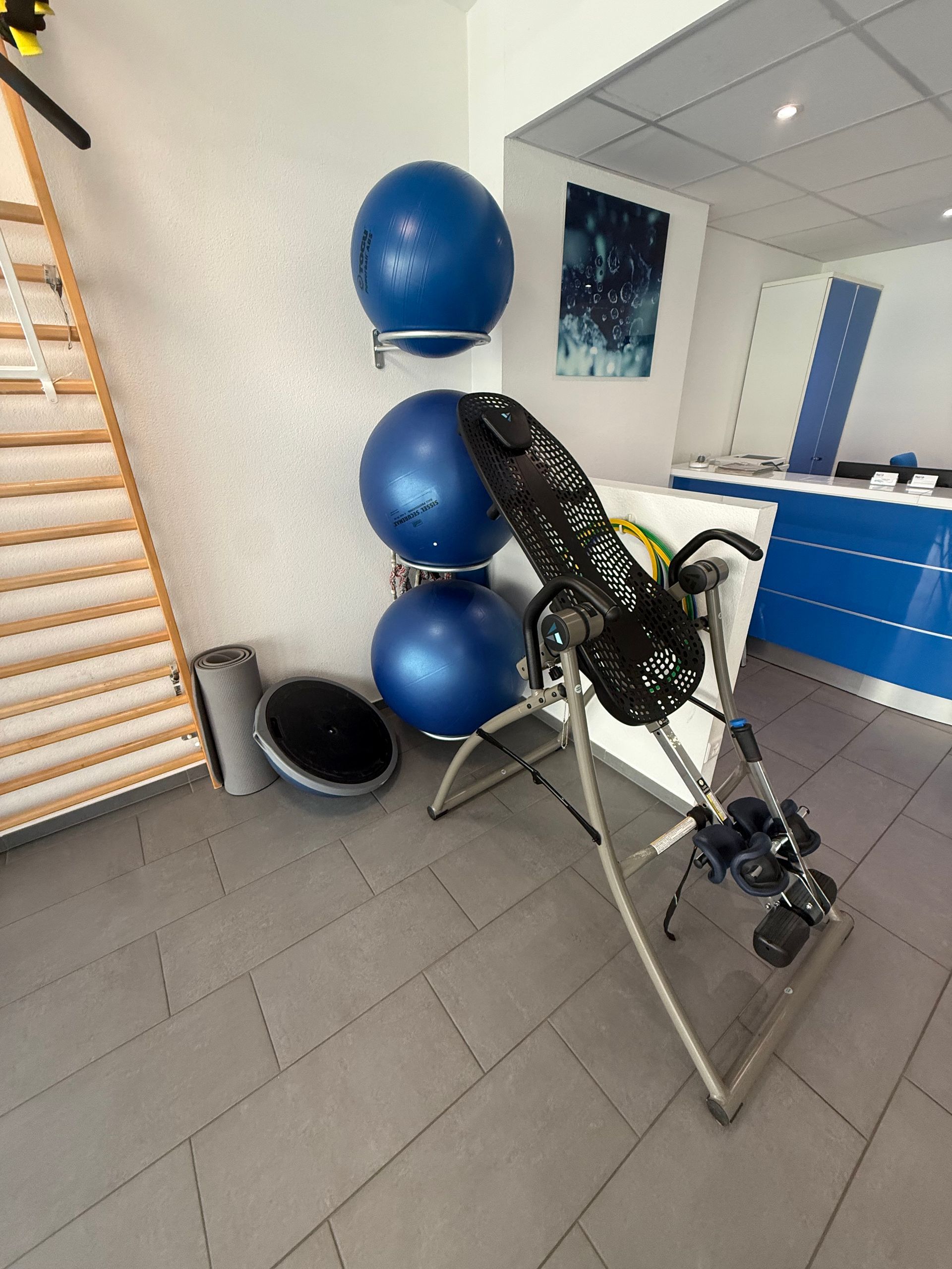 Coin gym avec ballons de stabilité bleus, appareils de musculation et barres murales sur un sol carrelé