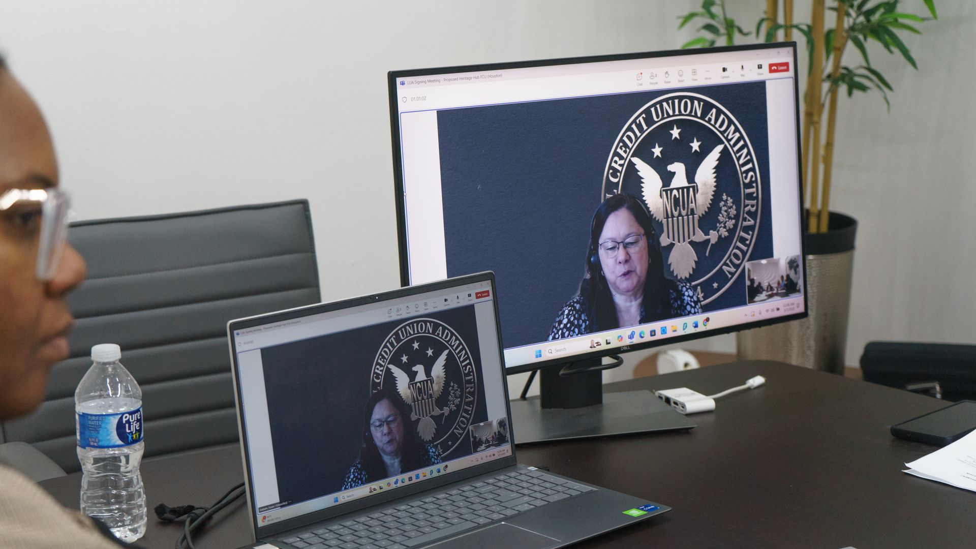 A person participates in a virtual meeting with a speaker visible on both a laptop and an external computer monitor.