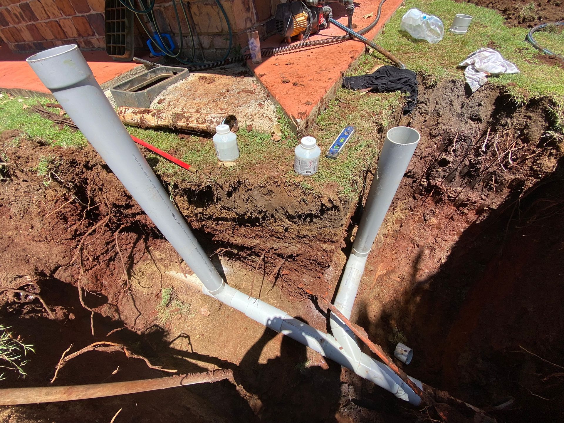 An Excavated Trench in a Yard Containing Grey Plastic Sewer Pipes — Truflow Plumbing & Gas Solutions in Rockhampton City, QLD