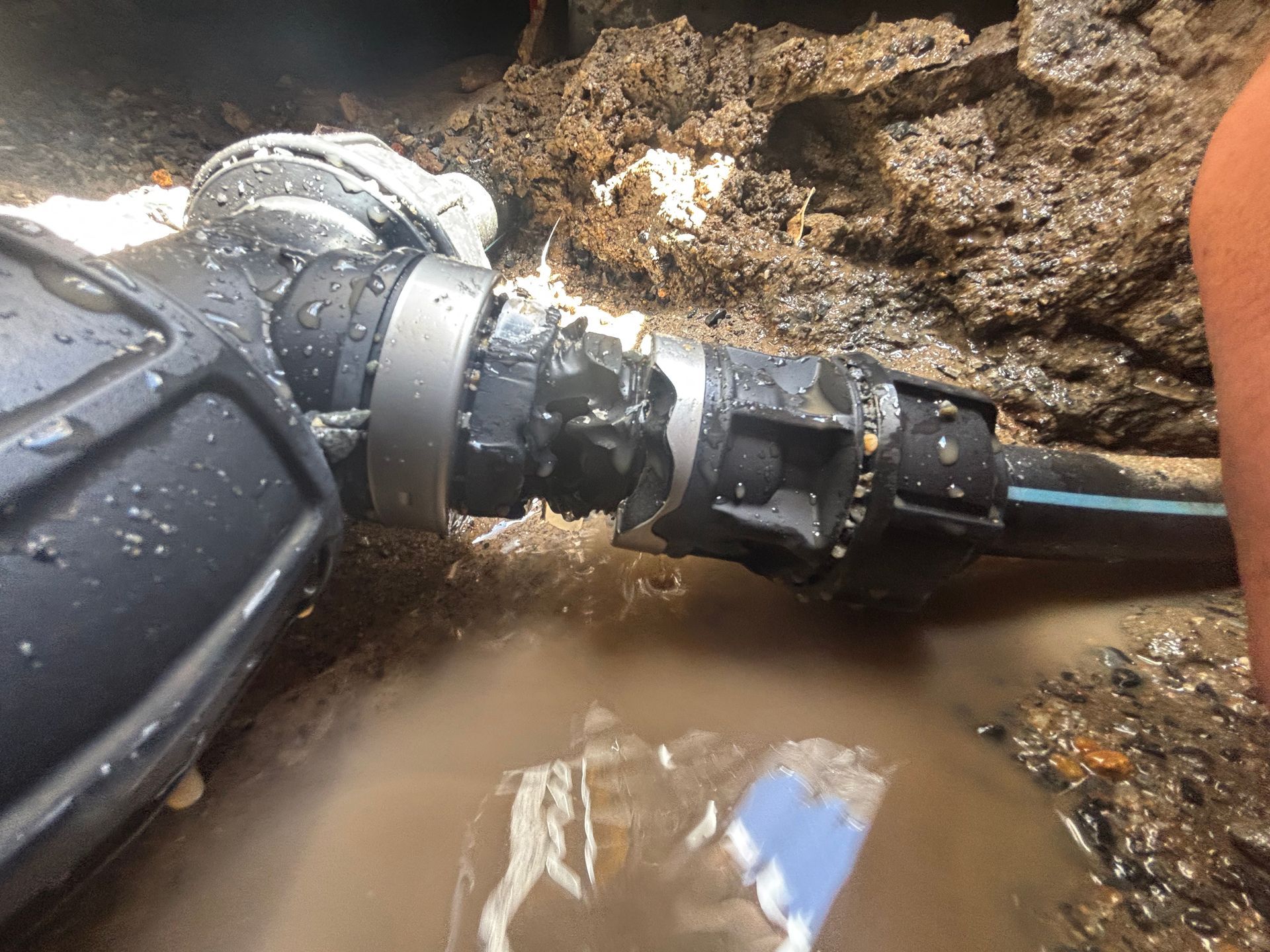 A gloved hand connects a black hose to a wet pipe — Truflow Plumbing & Gas Solutions in Rockhampton City, QLD