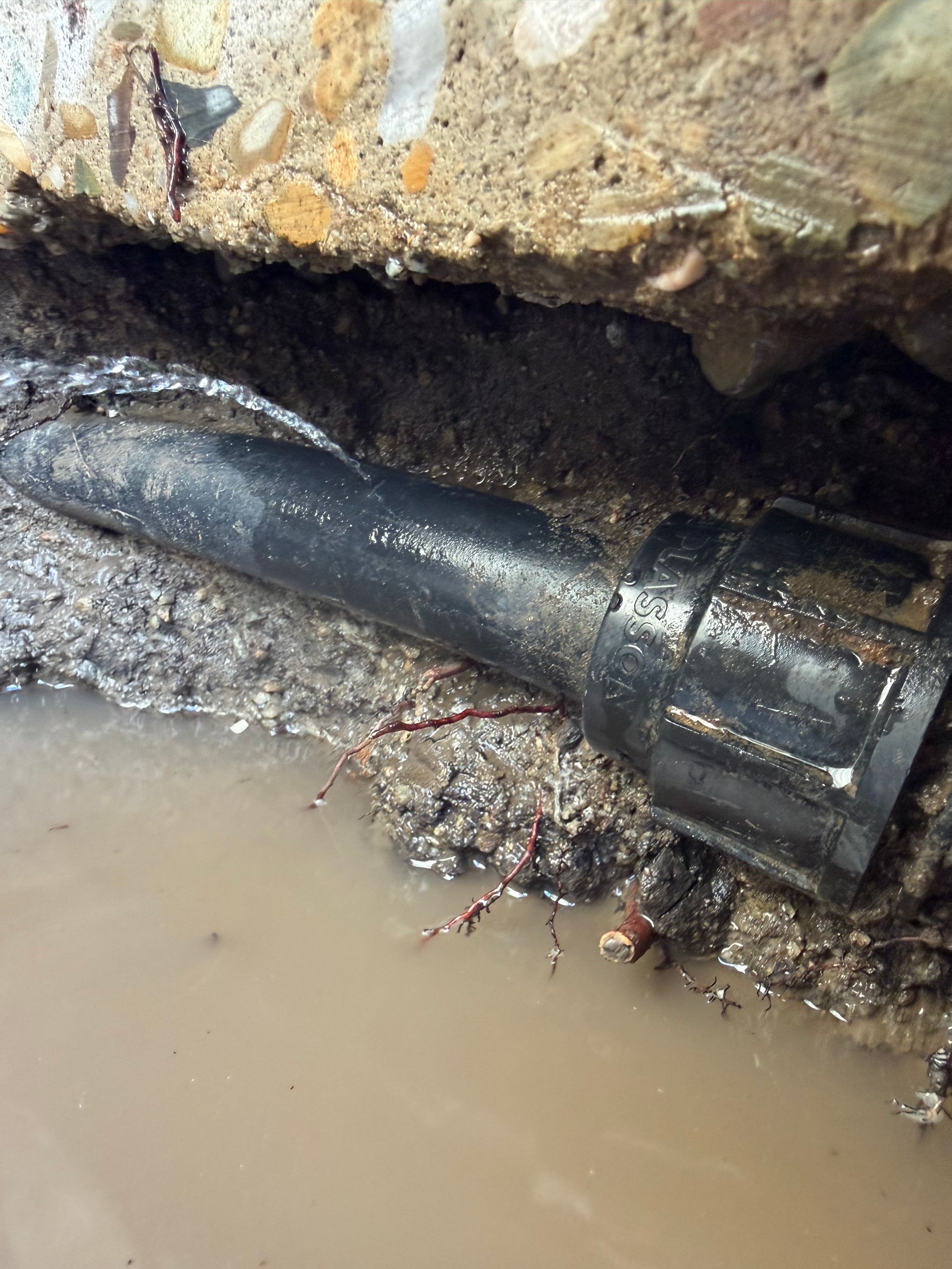 Black pipe or cable lying in muddy water under a rough rock ledge — Truflow Plumbing & Gas Solutions in Rockhampton City, QLD