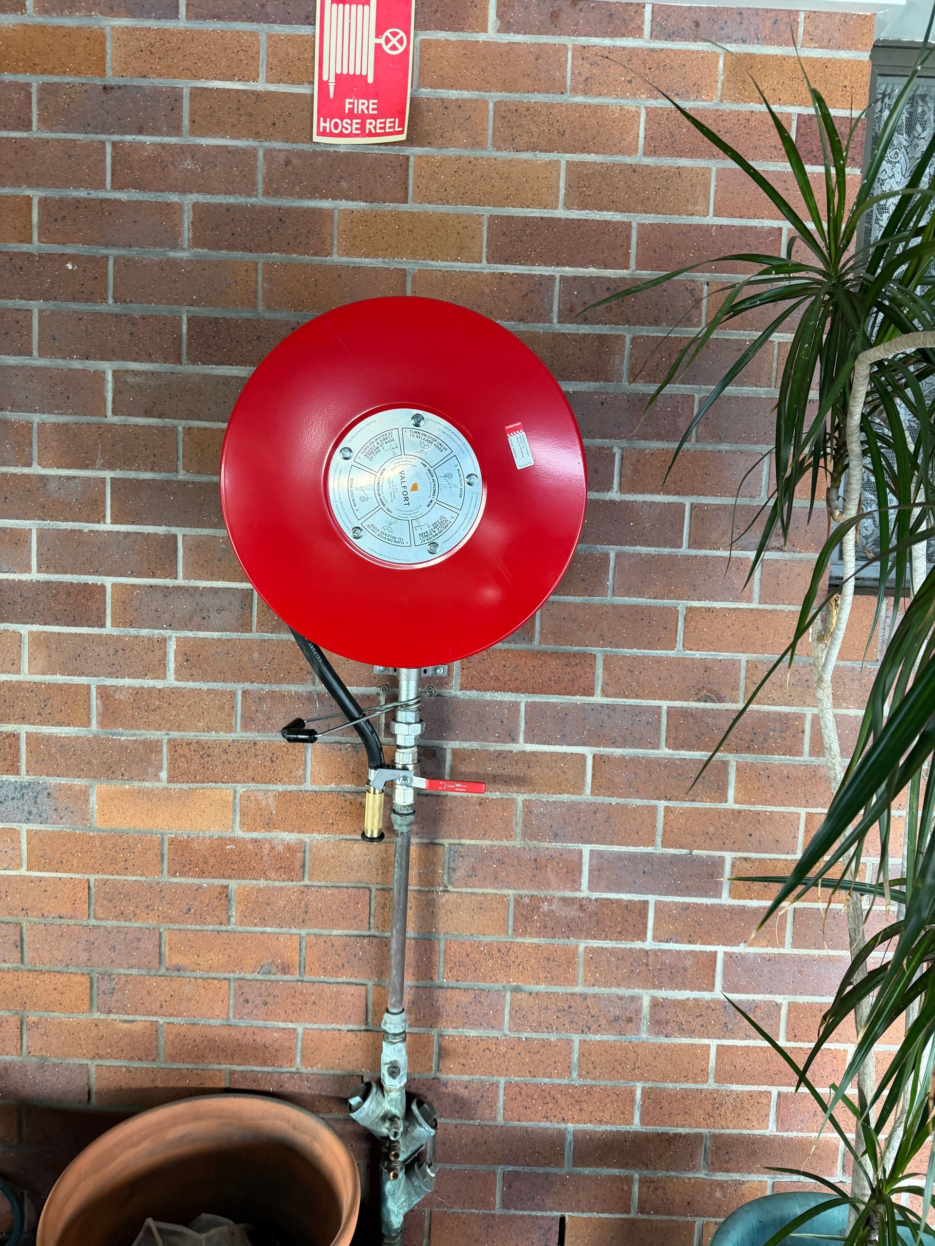 Red fire hose reel mounted on a brick wall near a potted plant — Truflow Plumbing & Gas Solutions in Rockhampton City, QLD