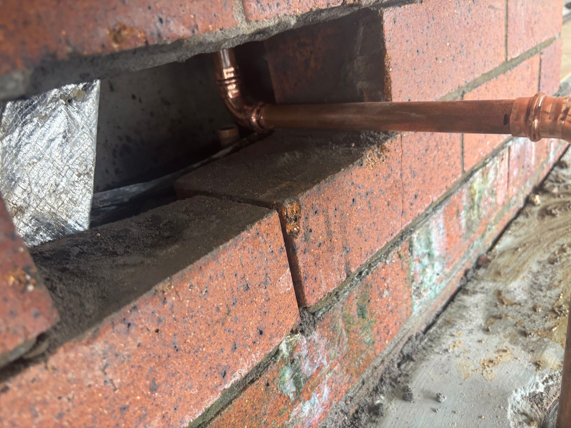 Copper pipe passing through a gap in a red brick wall near concrete ground— Truflow Plumbing & Gas Solutions in Rockhampton City, QLD