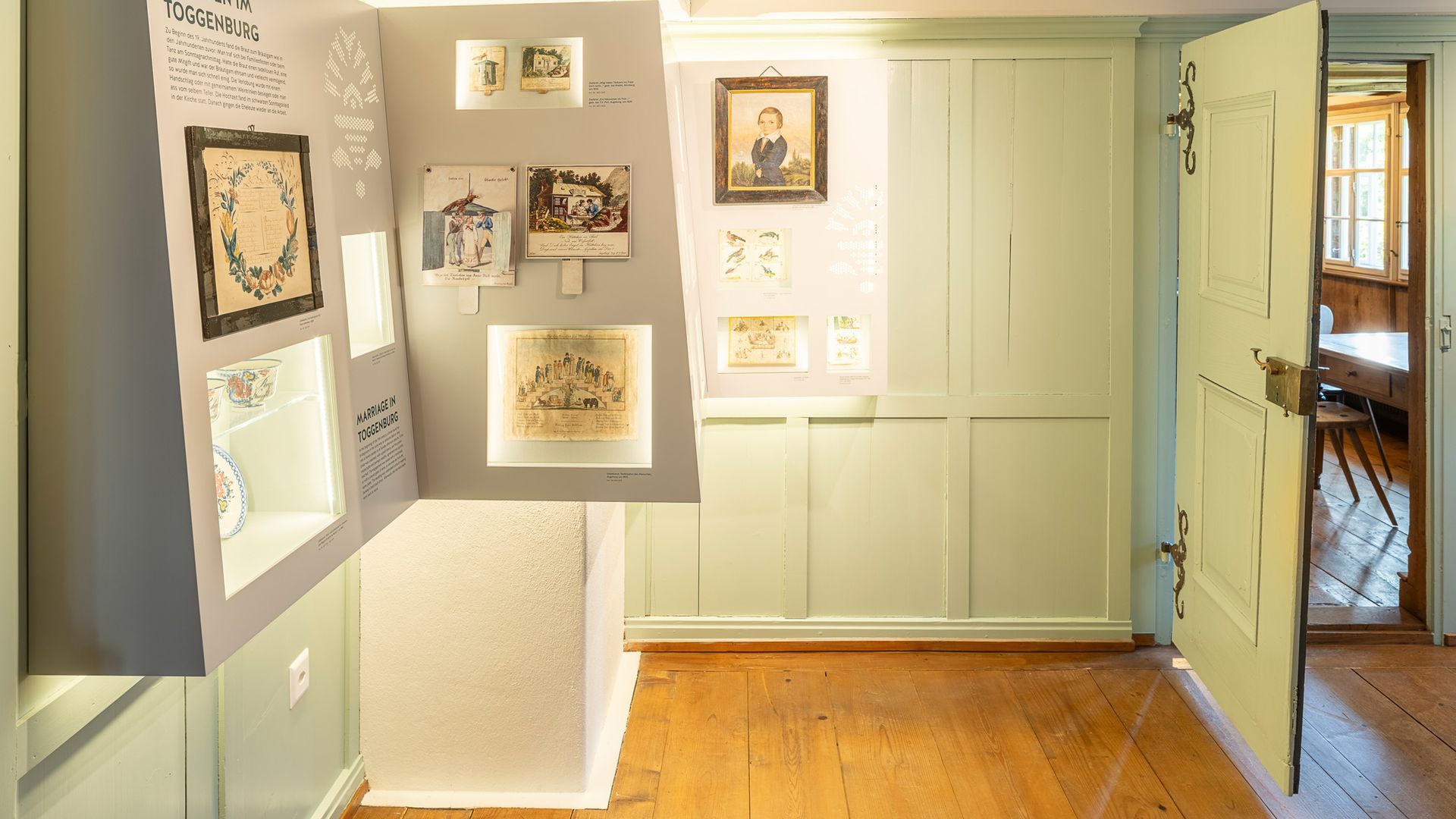 Ausstellung historischer Gegenstände in einem Raum mit hellgrünen Wänden und Holzboden.