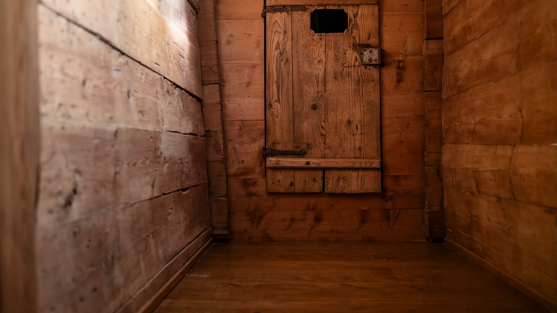 Holzvertäfelte Inneneinrichtung, schmaler Raum, Tür mit kleiner quadratischer Öffnung.