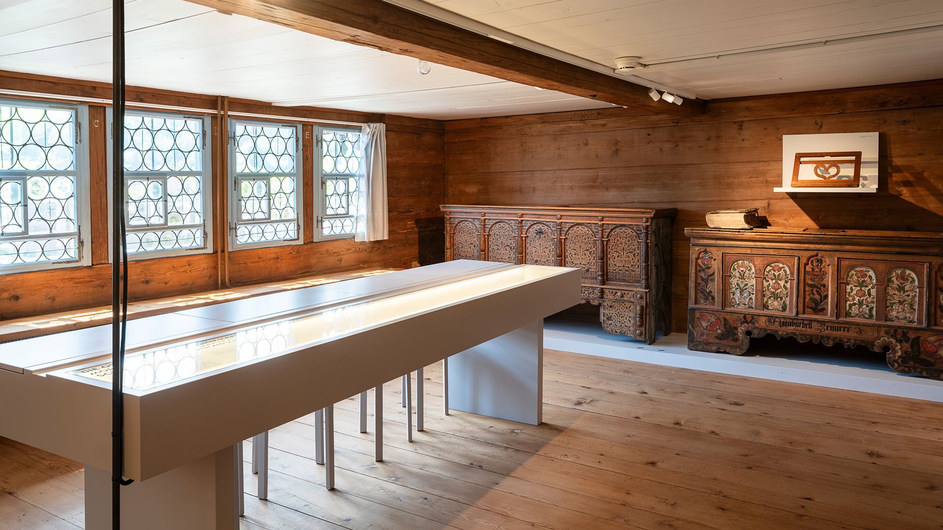 Ausstellungsraum im Museum Ackerhus mit historischen Truhen, Bauernmalerei und moderner Vitrine zur Toggenburger Wohn- und Alltagskultur