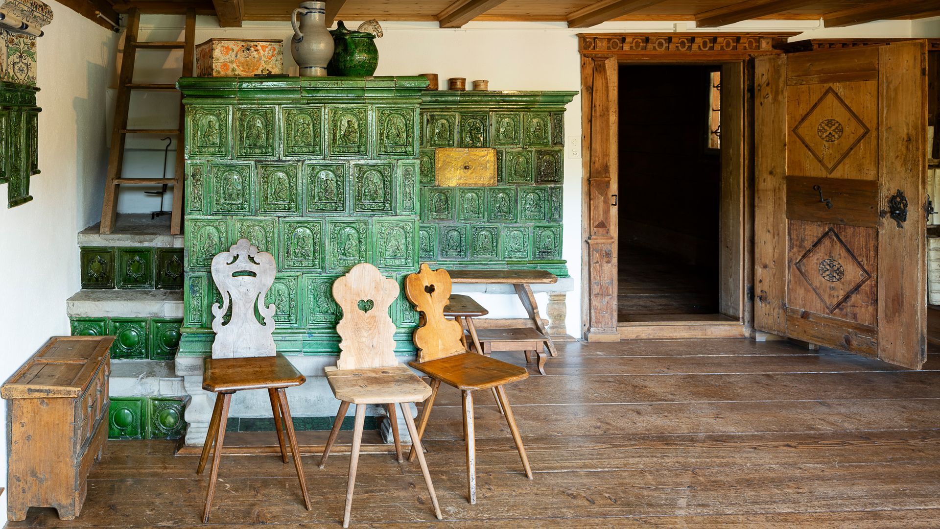 Historische Toggenburger Stube mit grünem Kachelofen und traditionellen Holzstühlen im Ackerhus