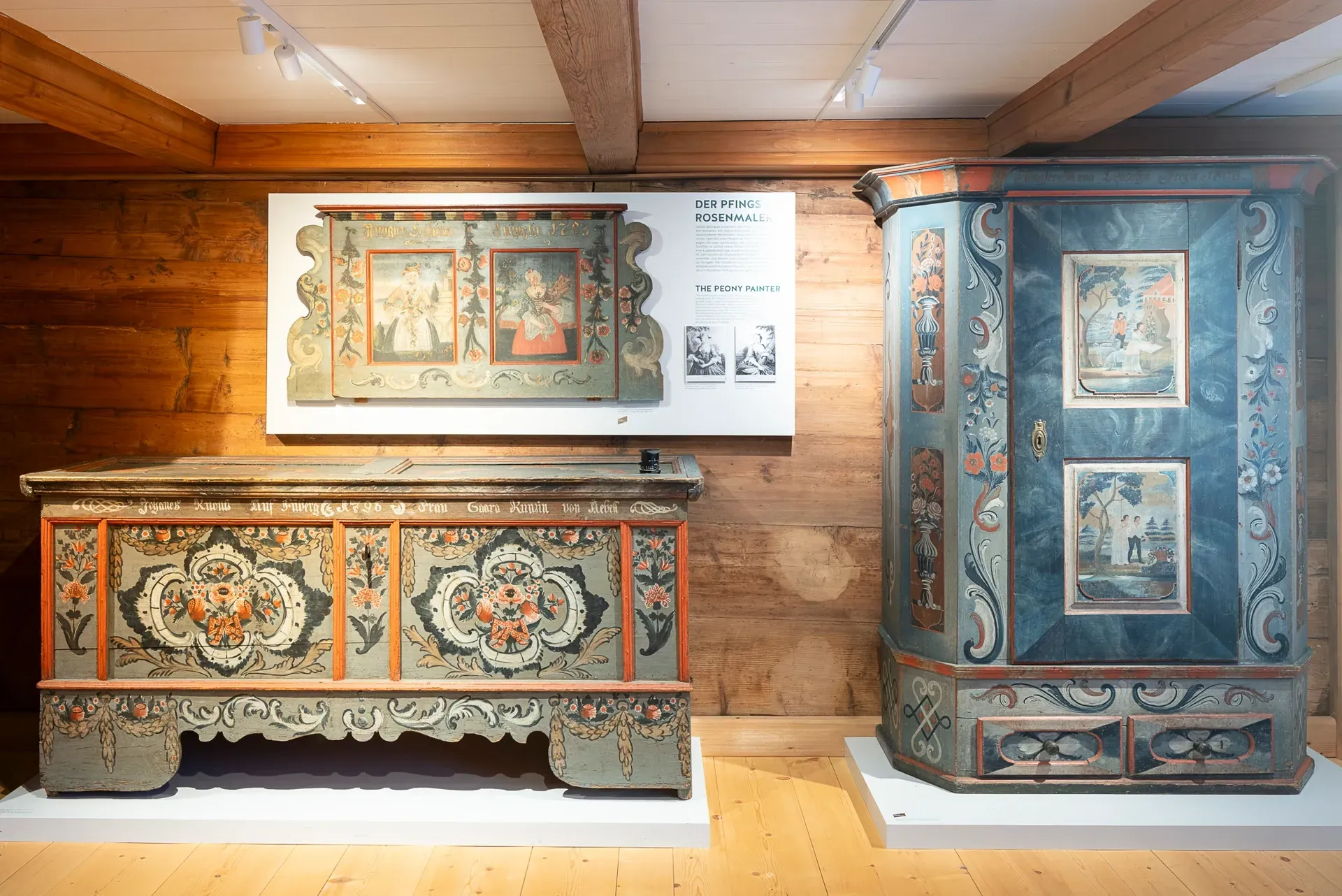 Holztruhen und Schränke mit bemalten Blumen- und Figurenmotiven, ausgestellt in einem Museumsambiente.