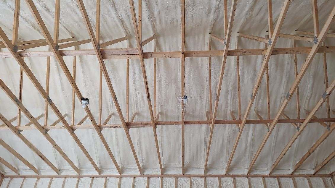 Wooden roof trusses with white spray foam insulation.