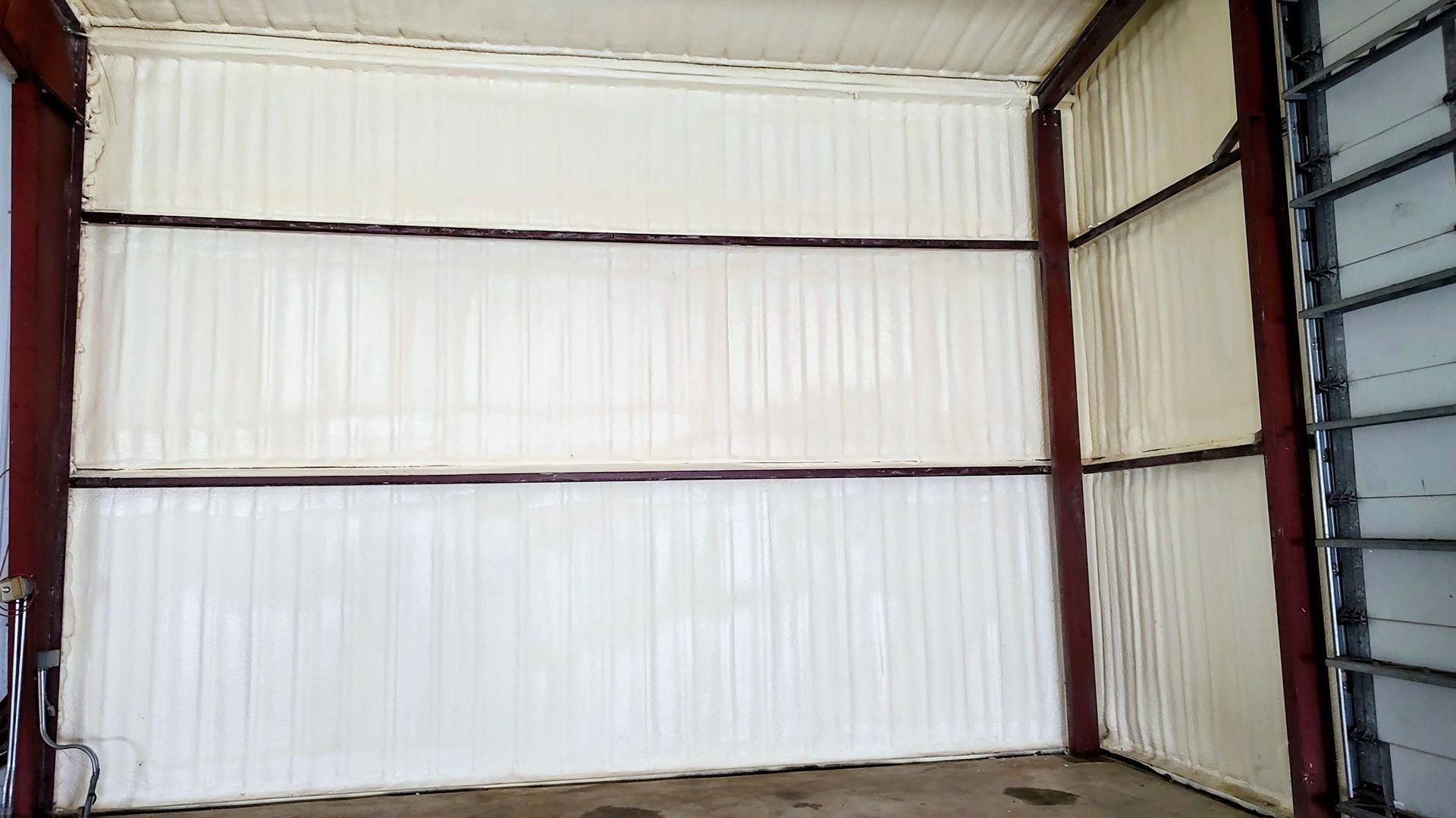 Interior of a metal building with white insulated walls, brown beams, and a dirt floor.