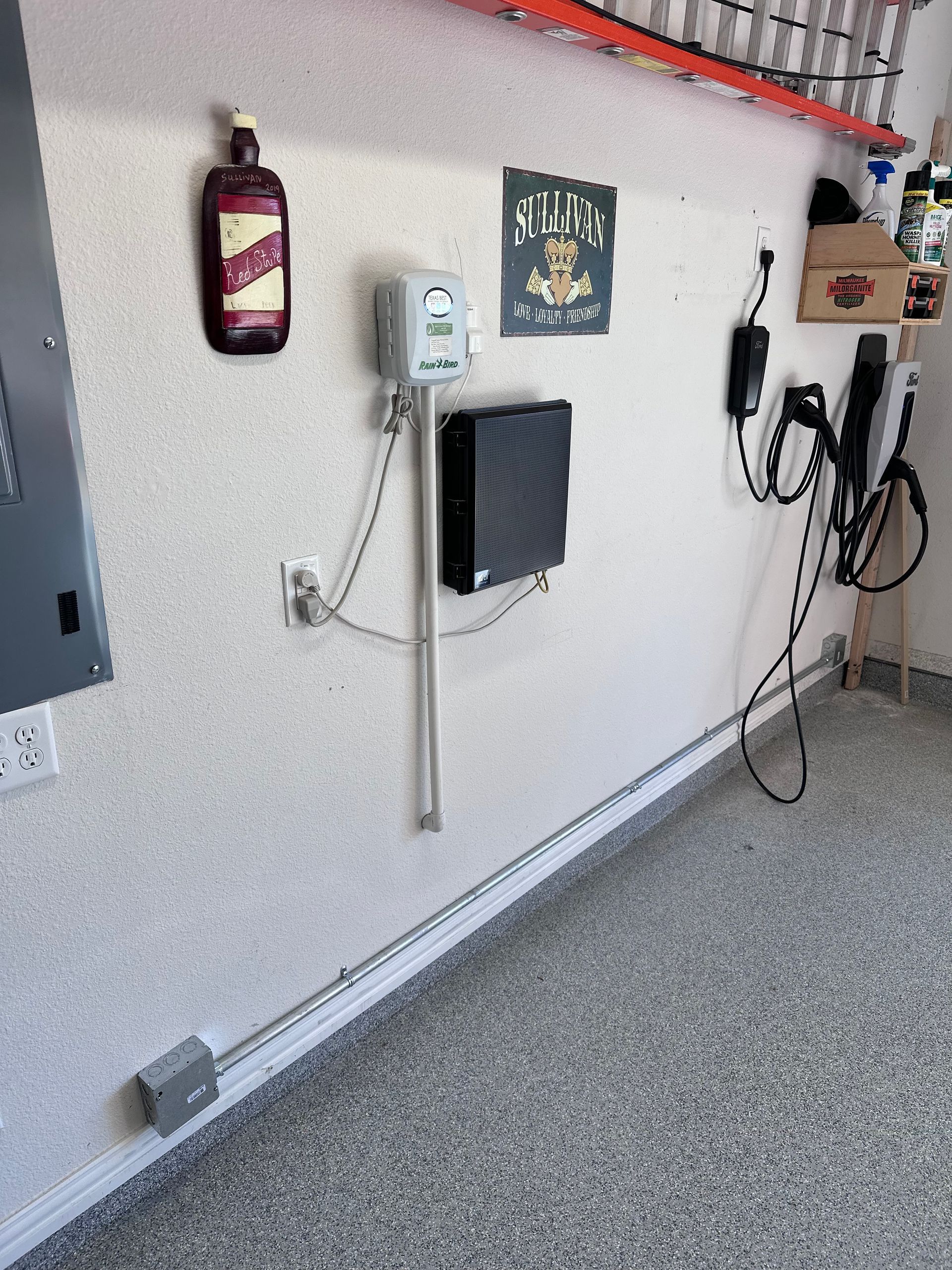 Garage wall with electrical panel, charger, and various objects.