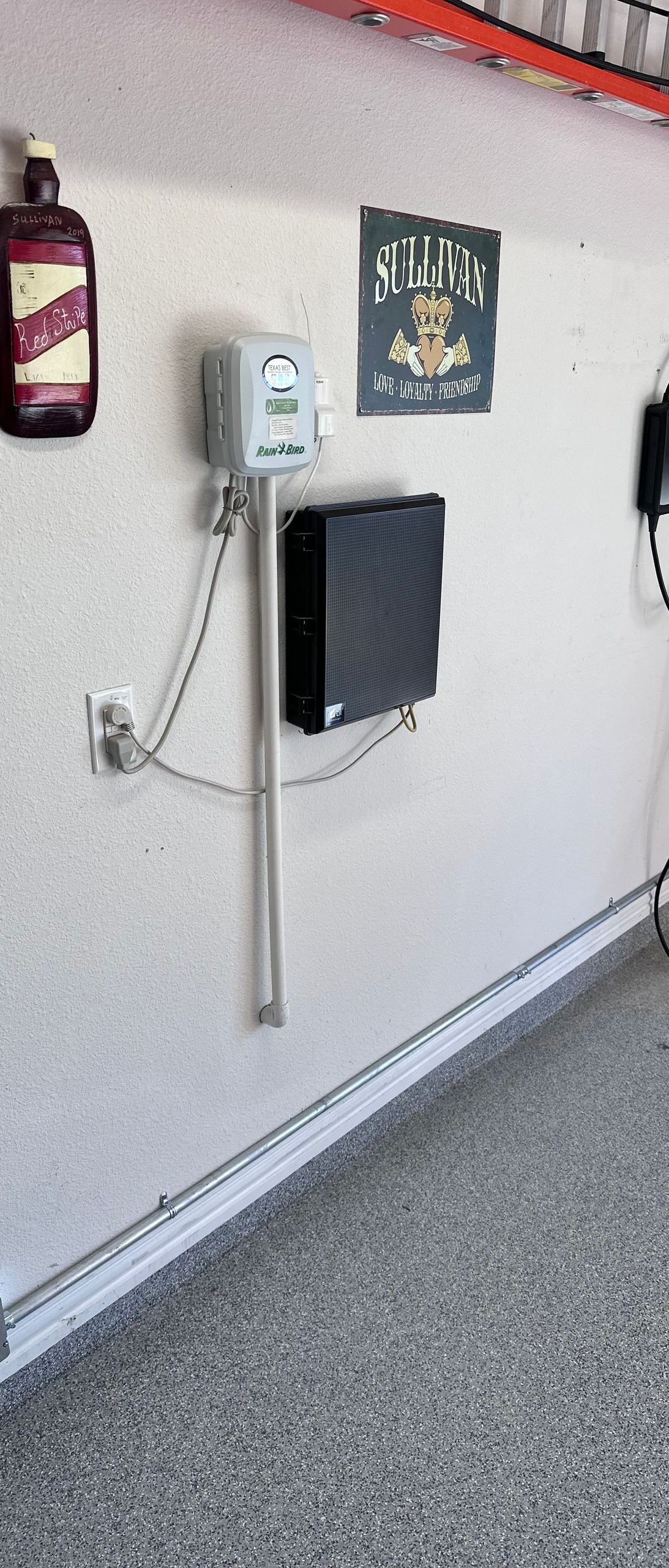 Garage wall with electrical panel, charger, and various objects. Includes a bottle and artwork.