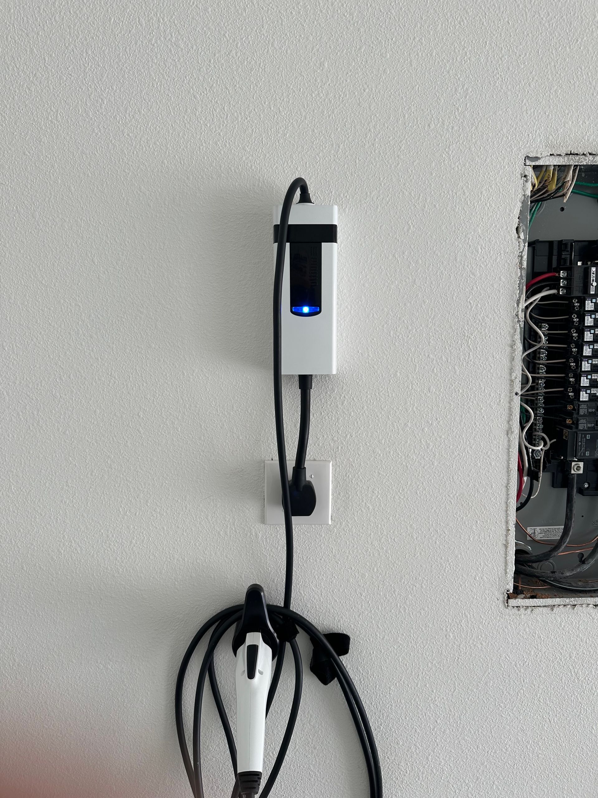 EV charger and plug installed on a textured wall next to an electrical panel.