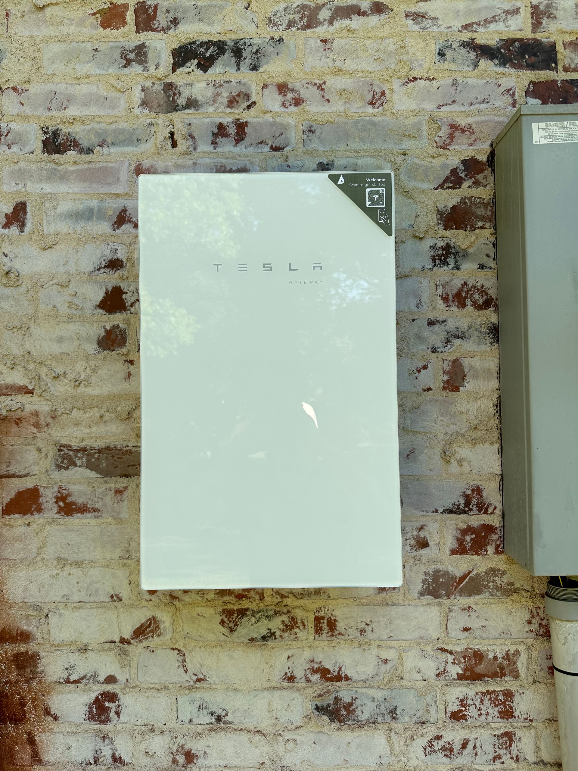 White Tesla Powerwall battery mounted on a red brick wall.