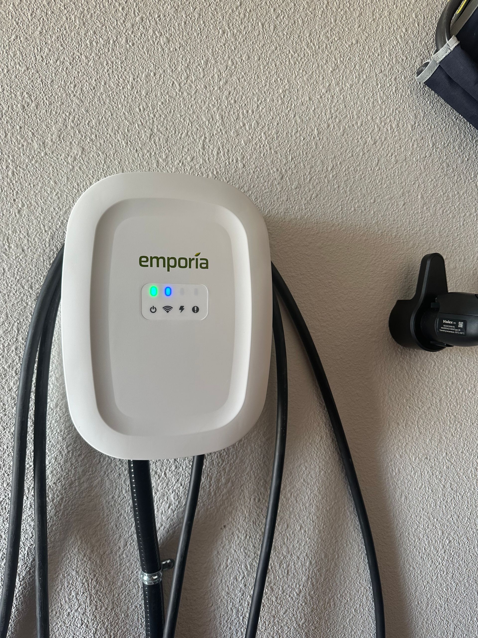 White Emporia EV charger mounted on a textured wall, with black charging cable and a detached charging handle.