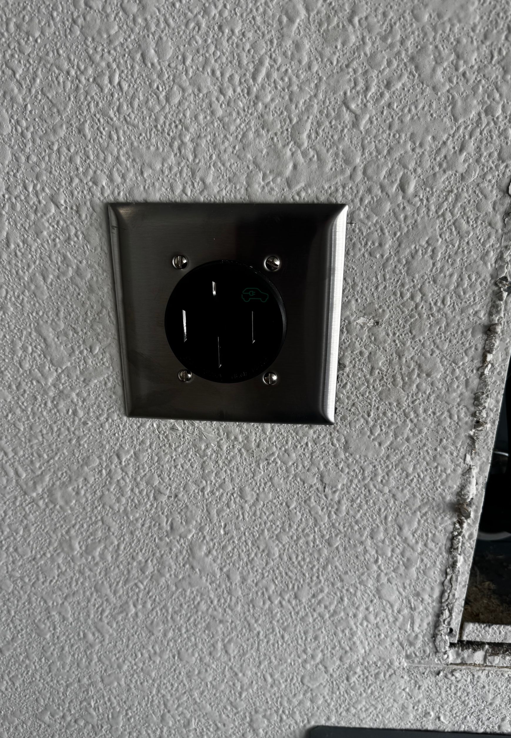 Black electrical outlet on gray textured wall, mounted in a metal plate.