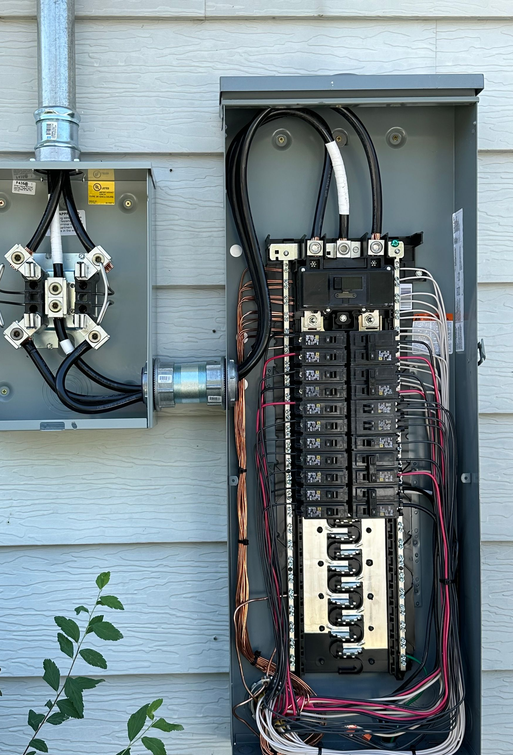 Exterior electrical panel with circuit breakers and conduit on a gray building.