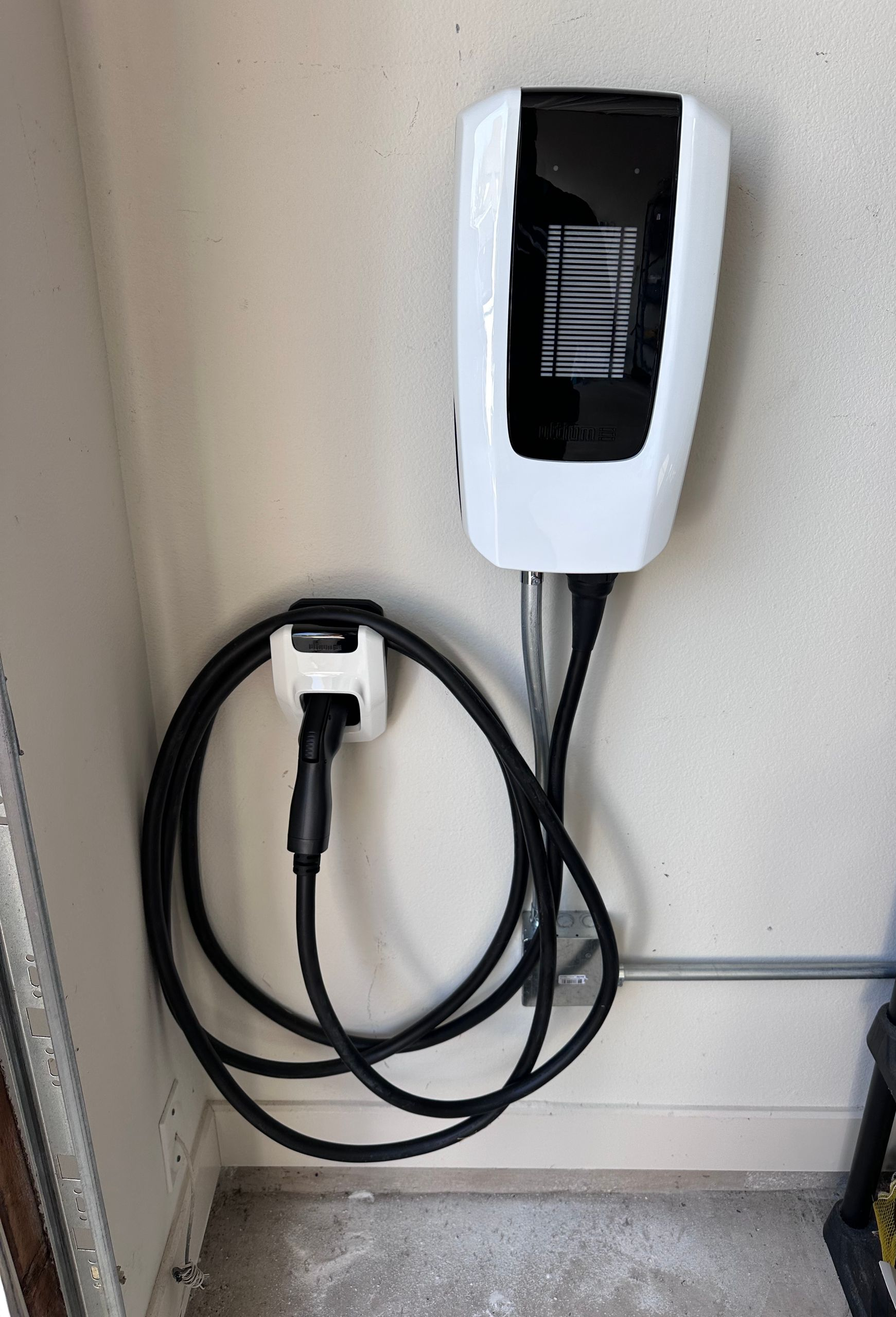 White electric vehicle charger mounted on a wall with black cable and connector.
