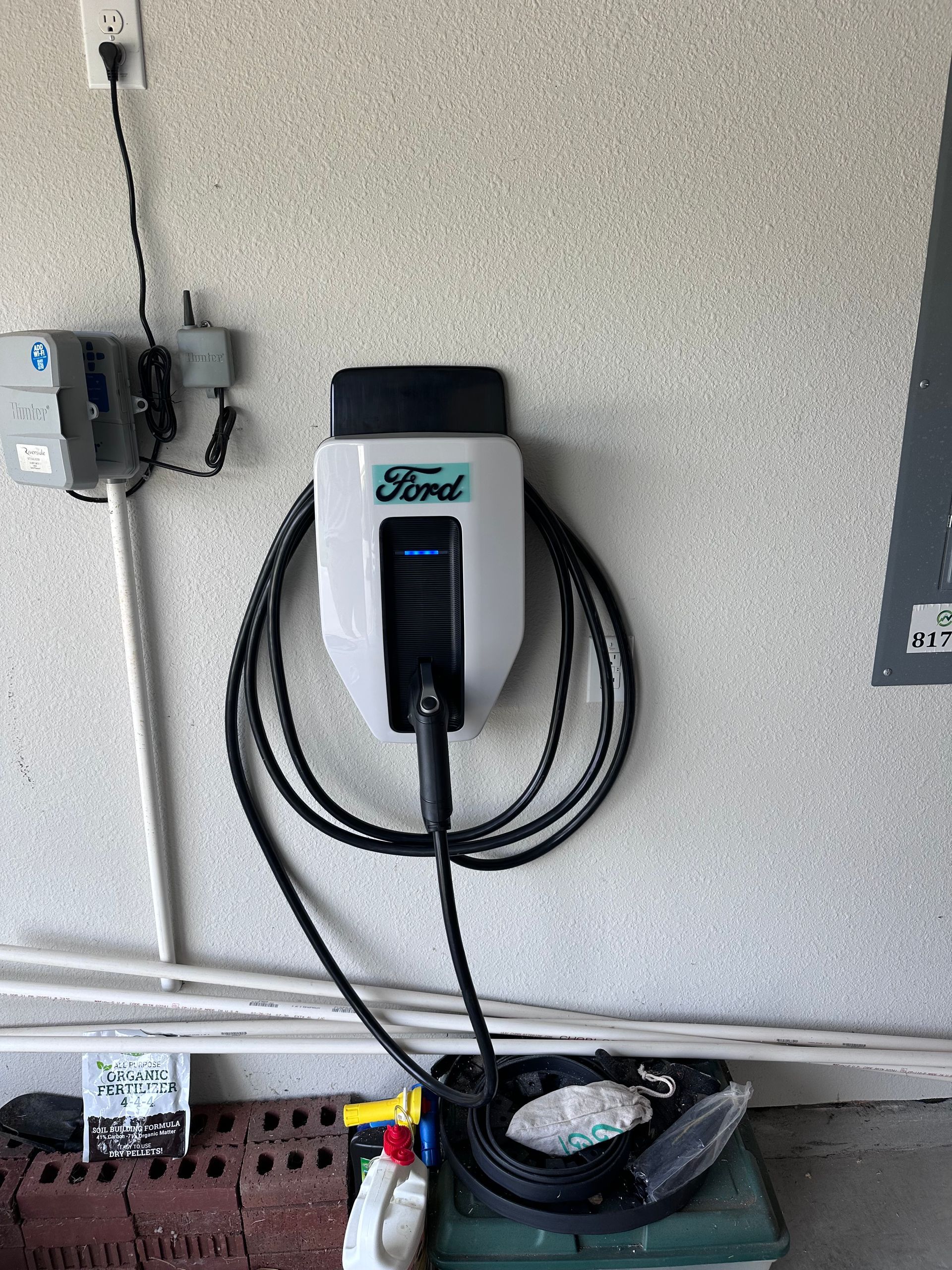 Ford EV charger mounted on a garage wall, with cable coiled and attached. Gray, white, and black.