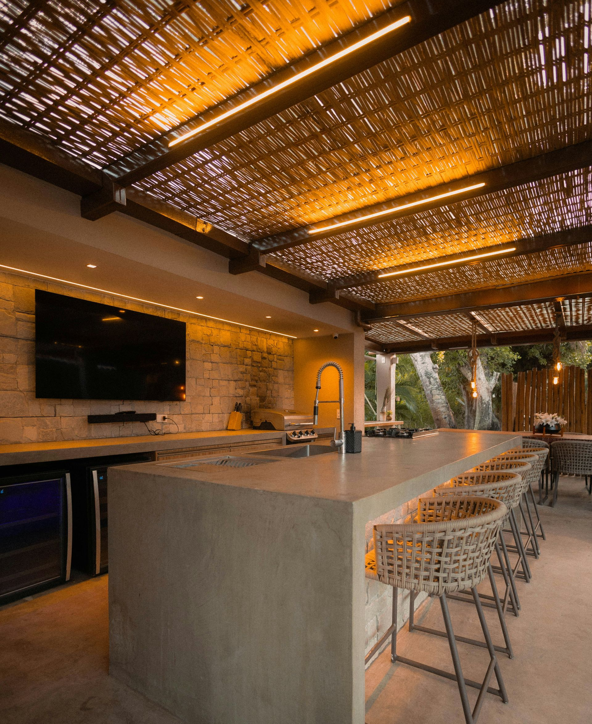 Outdoor bar with concrete counter, woven bar stools, and a bamboo ceiling.