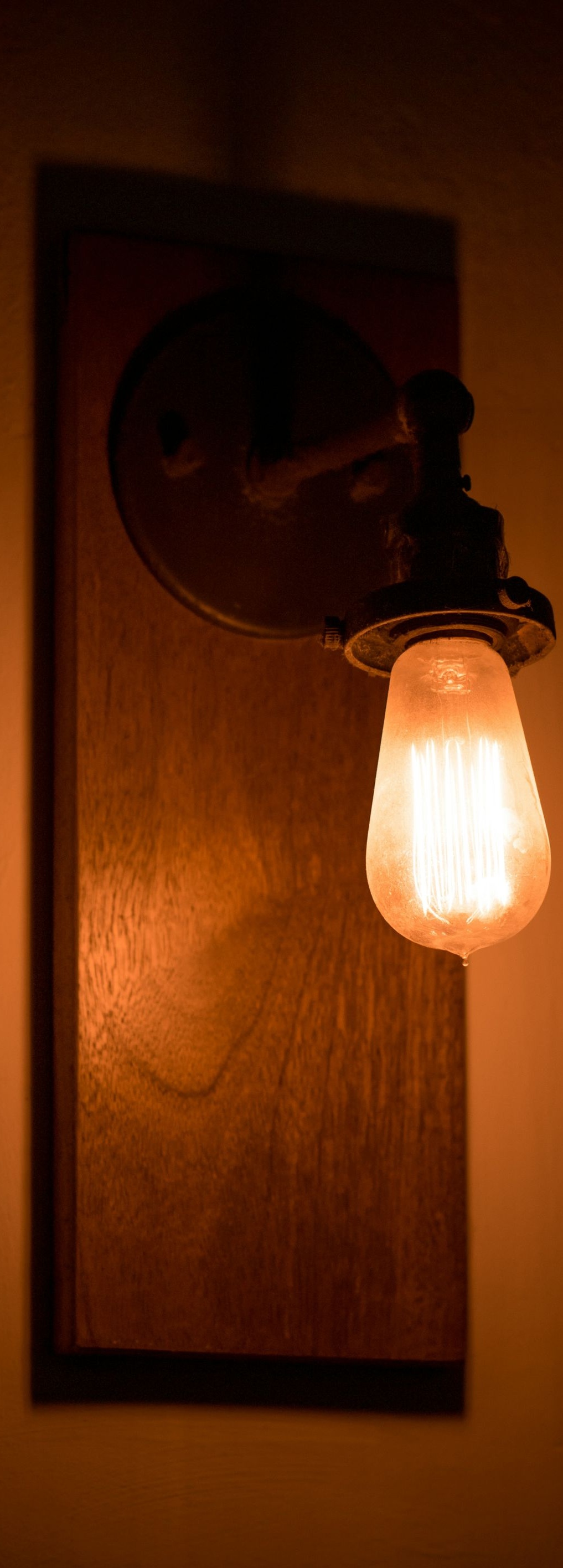 Wall-mounted light fixture with a glowing bulb and wooden backboard casting shadows.