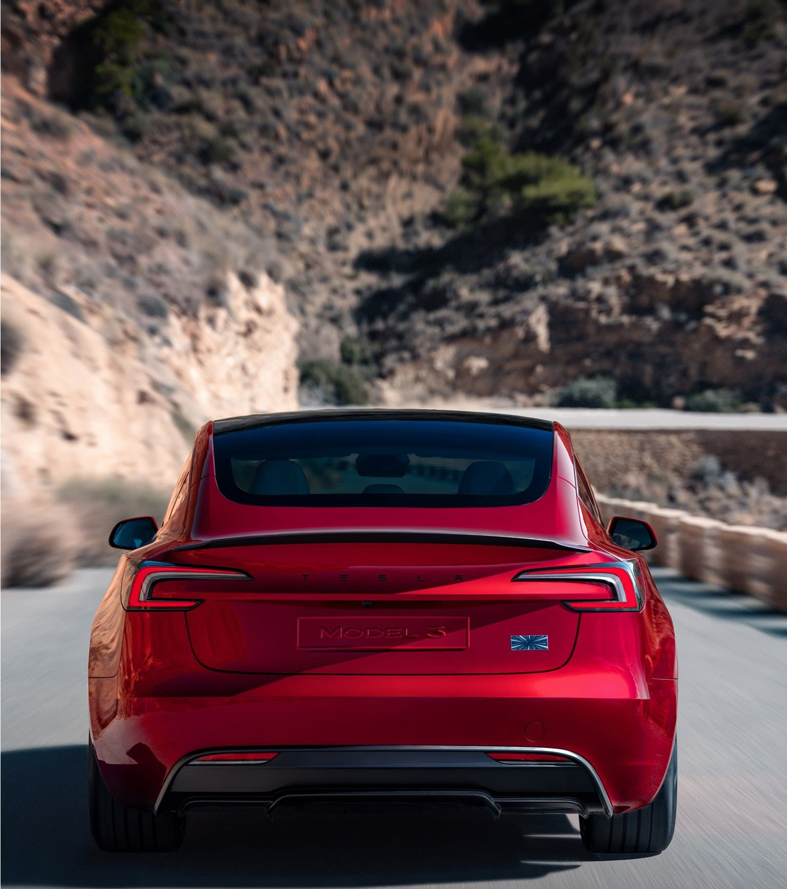 Red Tesla car driving on a mountain road with a blurred background.
