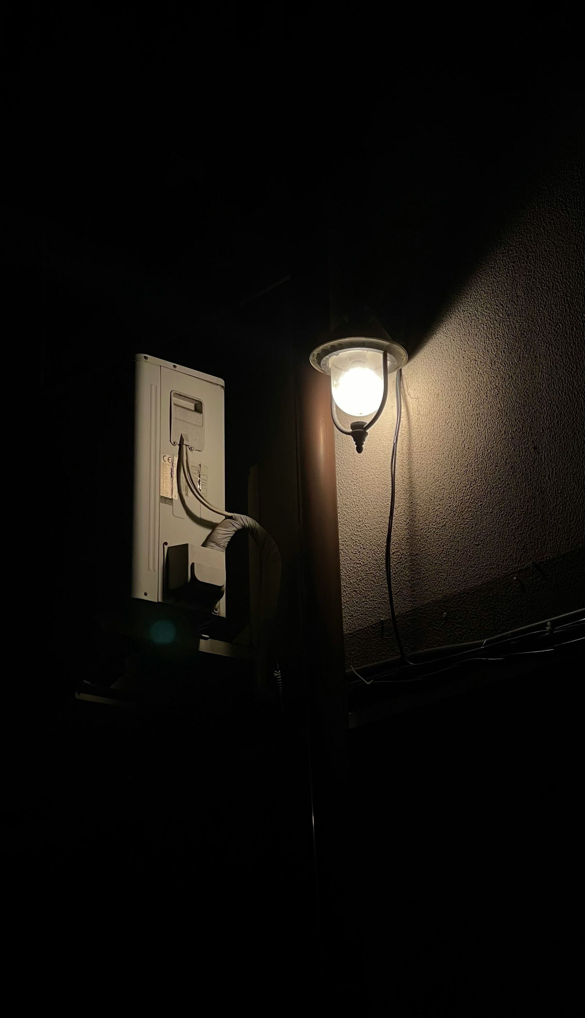 Street light illuminates a wall with a white panel and equipment at night.