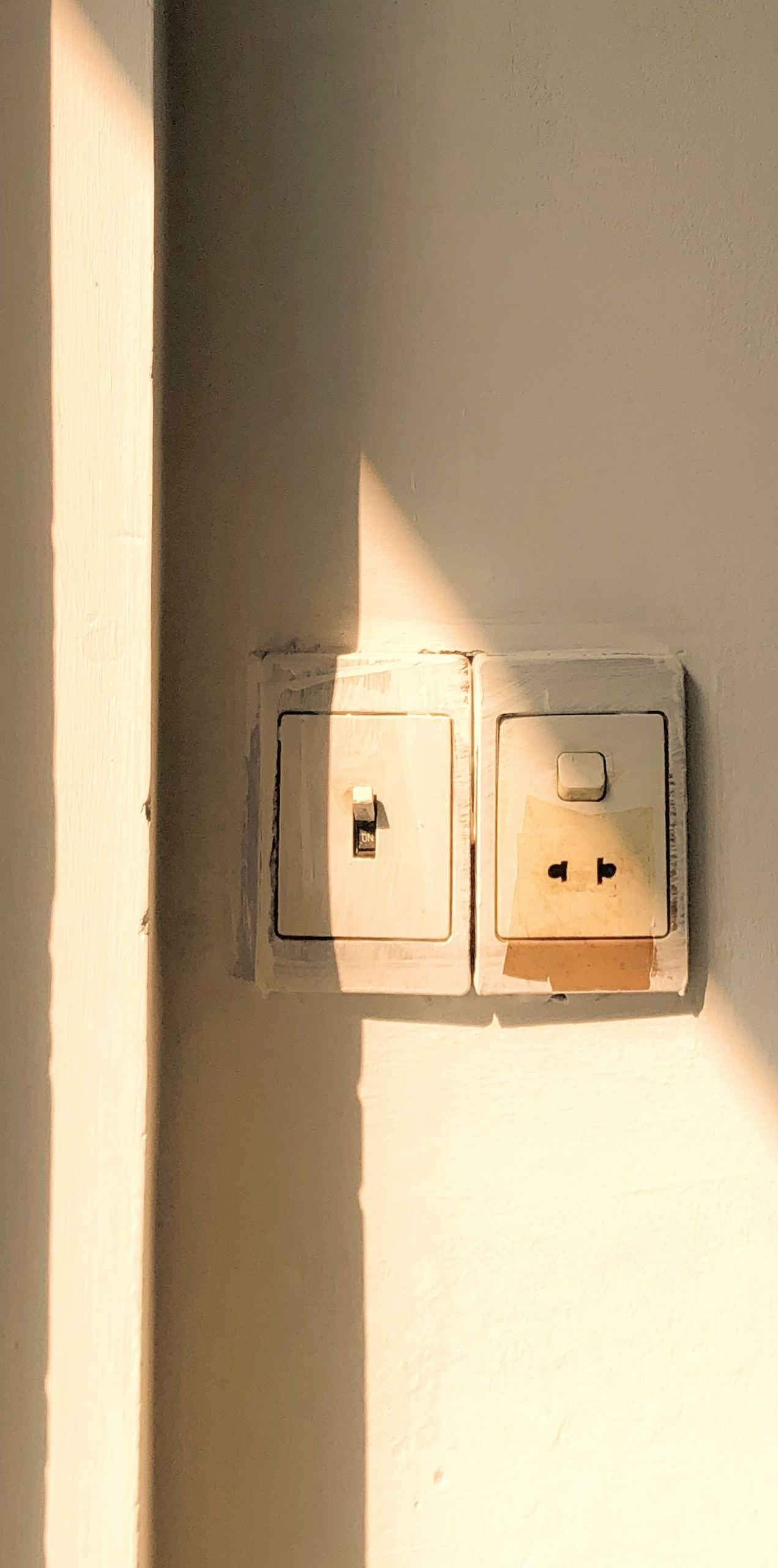 Electrical outlet and light switch on a white wall, lit by warm sunlight.