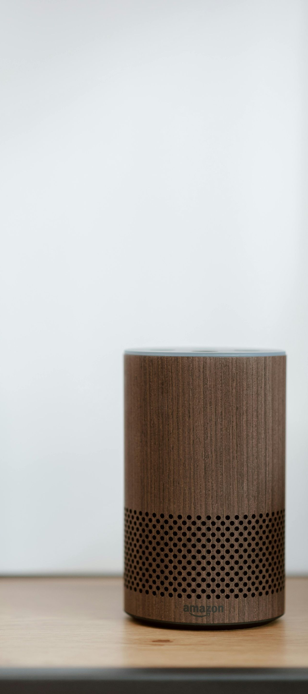 Smart speaker with a wood-grain finish sits on a shelf against a white wall.