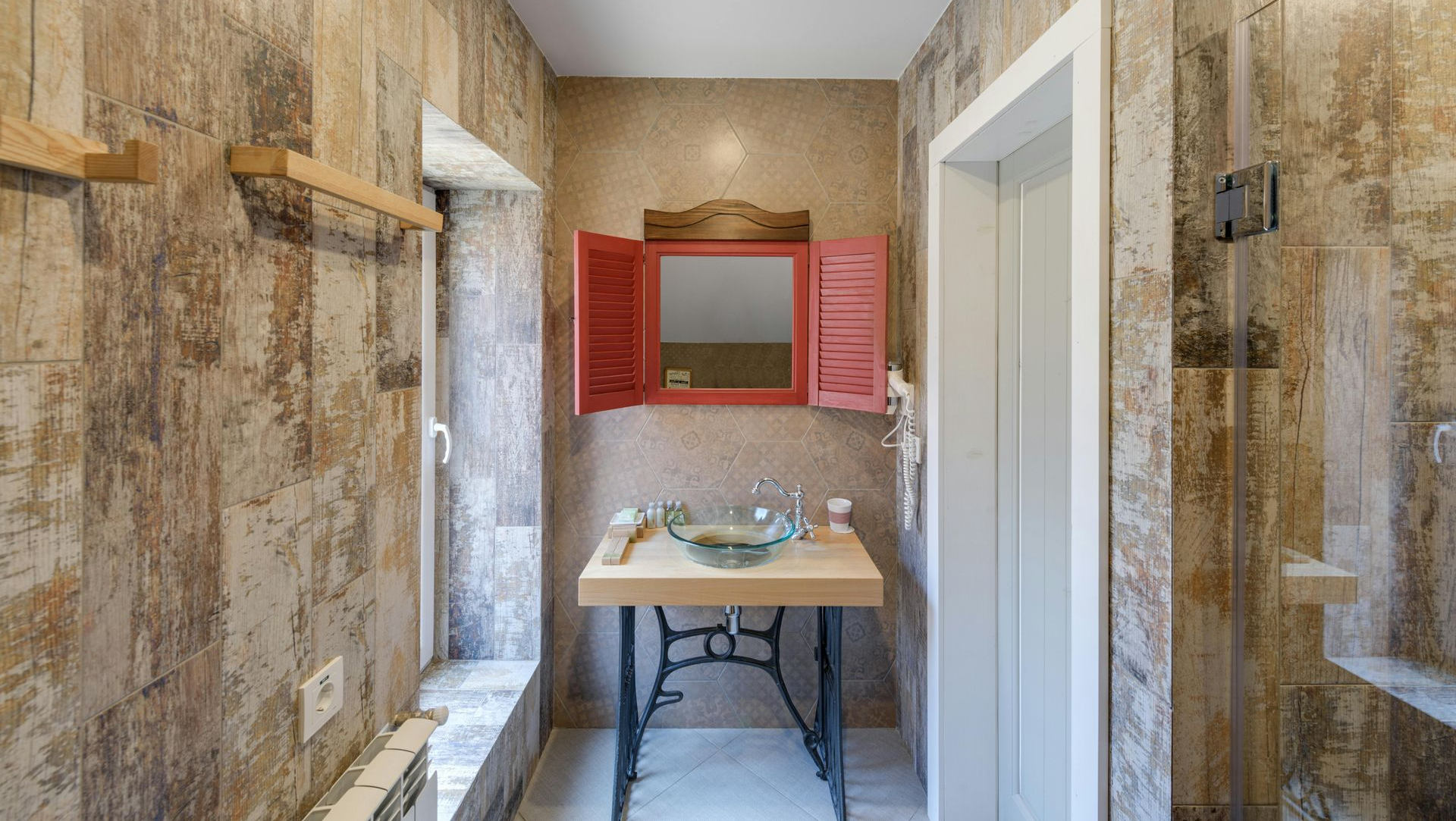 A bathroom featuring stone-tiled walls, a pedestal sink with a glass bowl on a vintage sewing machine base, and a mirror.