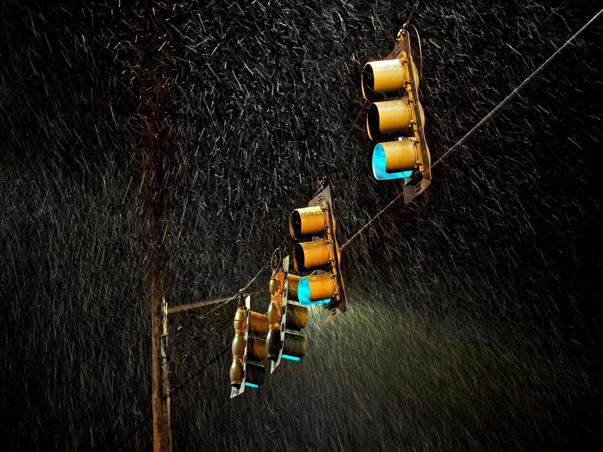 Traffic lights in the rain at night; green lights illuminated, brown poles, dark background.