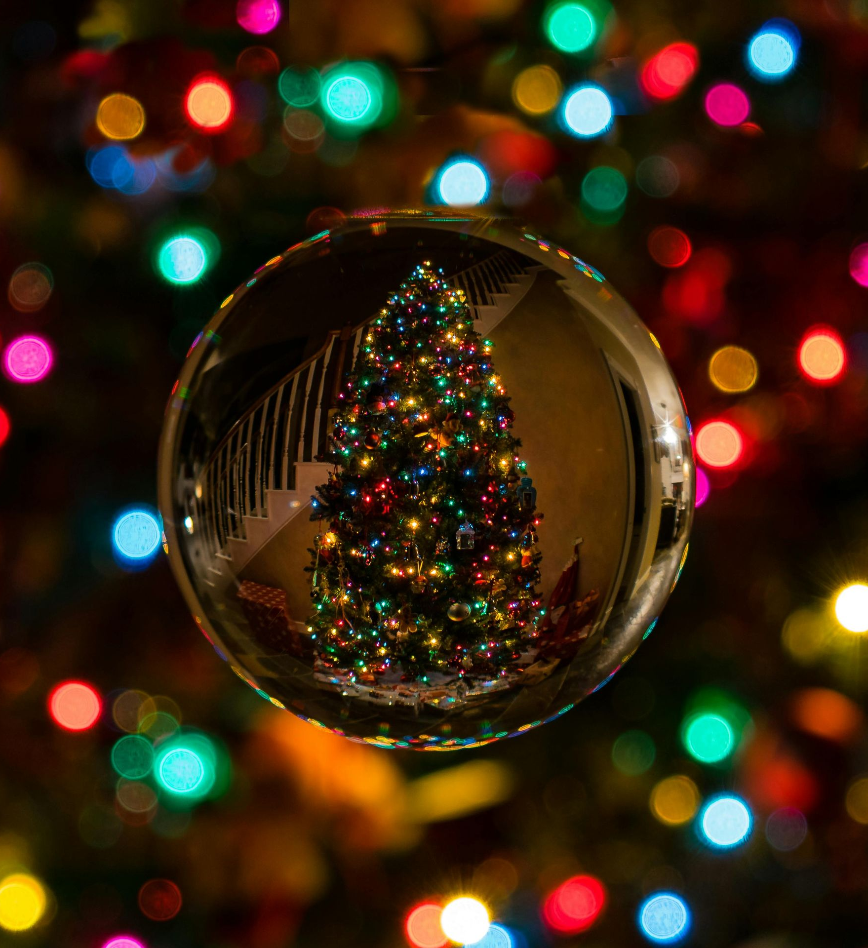 Christmas tree lights reflected in a crystal ball, surrounded by colorful bokeh.